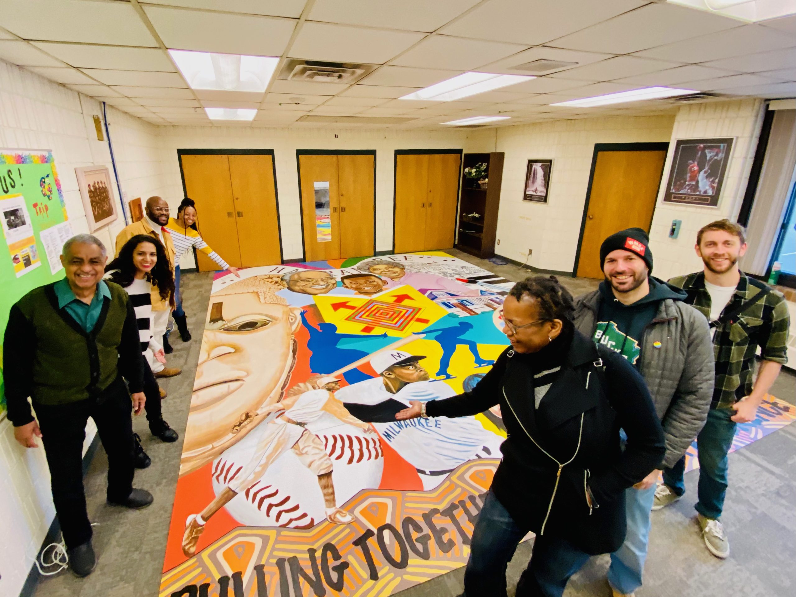 A group of people smiling while presenting a mural