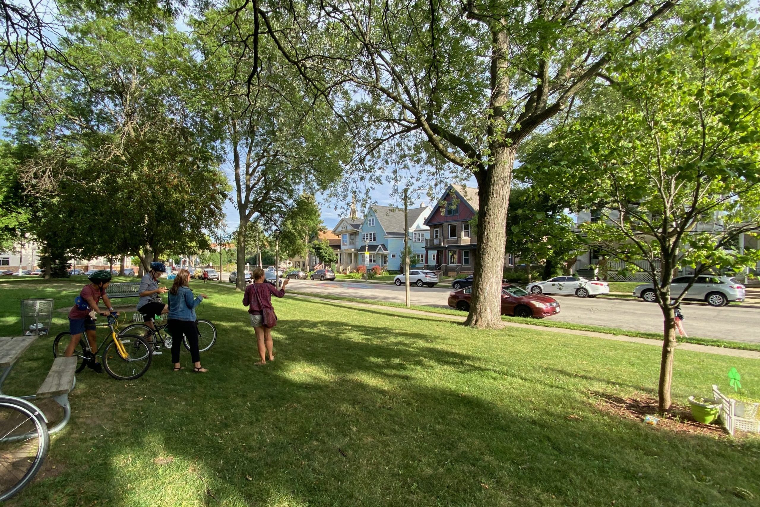 Ciclistas y paseantes en un parque conversando bajo los árboles