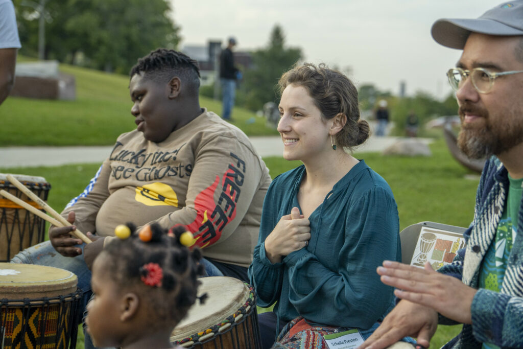 three adults and a young child playing drums in the park